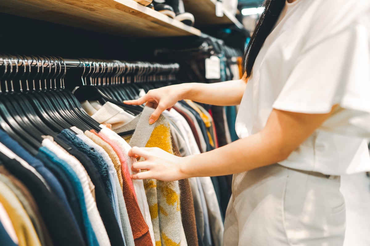 Woman arm choosing clothes from hangers in second hand clothing shop